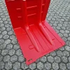 Eine große rote Kunststoff-Hochwasserschutzwand mit Rillen steht auf sechseckigen Pflastersteinen.
