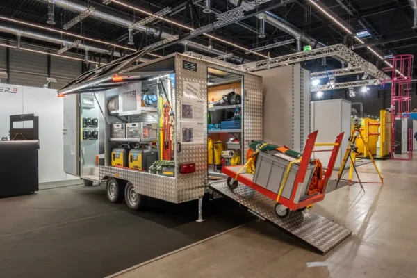 Ein gut beleuchteter Geräteanhänger mit offenen Fächern zeigt Hochwasserschutz-Equipment und Pumpen in einer Ausstellungshalle.