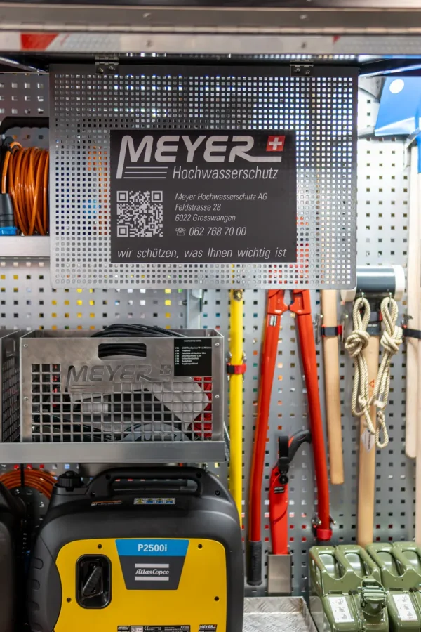 Lagerraum mit Seilen, orange Kabel, Schaufeln, Meyer Hochwasserschutz-Equipment und Infoschild mit QR-Code und Kontaktdaten.