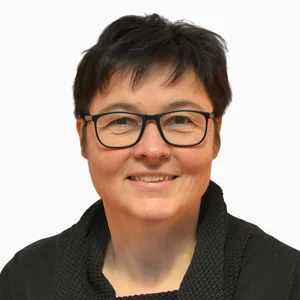 Eine Frau mit kurzen dunklen Haaren und Brille lacht, trägt ein schwarzes Top, vor weissem Hintergrund, Porträt Hochwasserschutz.